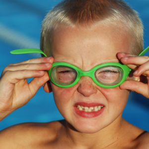 Little boy with swimming goggles squinting into the sunshine.