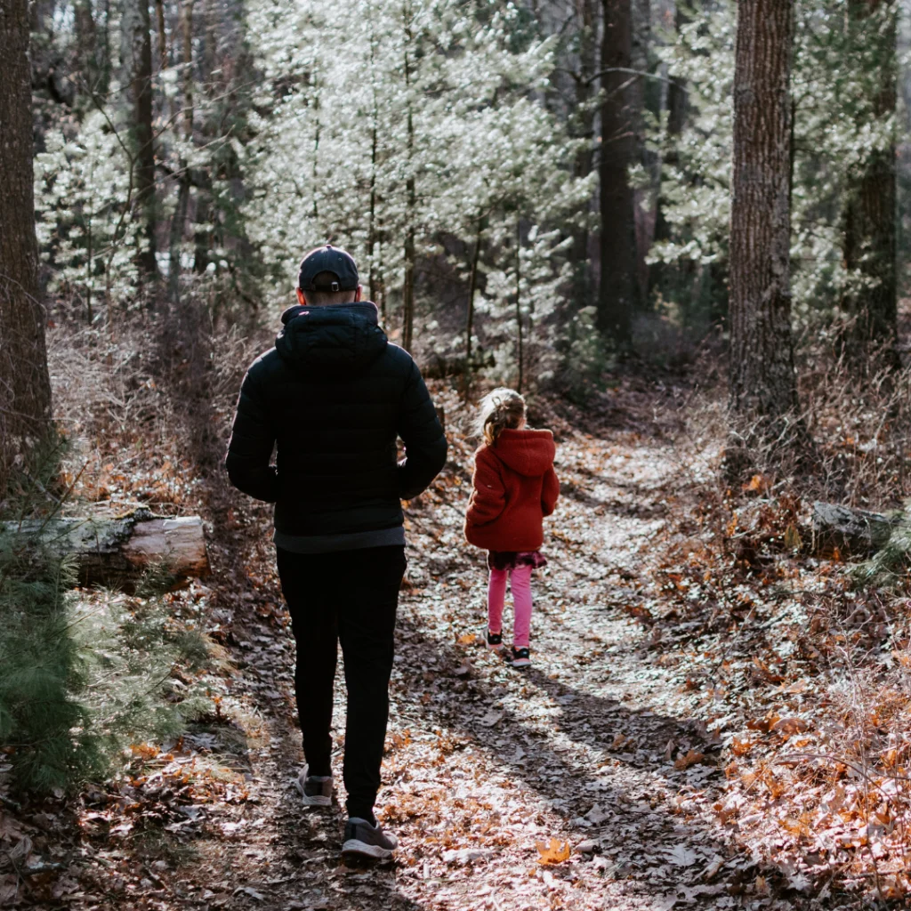 Man and child walking together on forest trail in autumn.